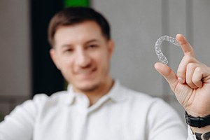 Man holding Invisalign aligner between his thumb and forefinger