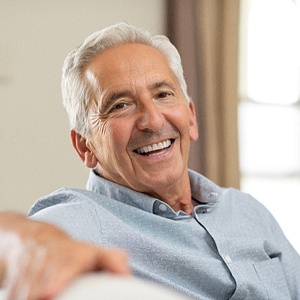 Senior man on couch smiling to show dentures in Northborough