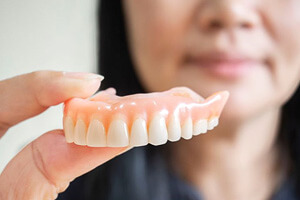 womans hand holding denture for upper arch