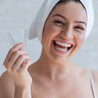 Smiling woman holding mouthguard to prevent dental emergencies in Northborough