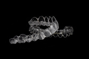 Two Invisalign clear aligners arranged against dark background