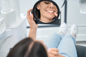 Dental patient looking at her gums in hand mirror
