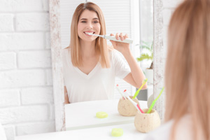 Woman brushing her teeth in front of bathroom mirror