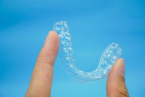 Hand holding clear Invisalign retainer in Northborough against blue background
