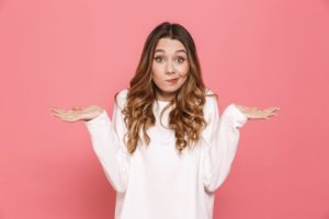 Woman in white sweater, shrugging with confused expression on face